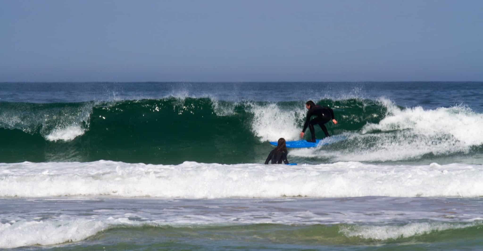 a surfer learning to surf on a wave and another person watching from the water